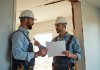 Expert en construction et propriétaire examinant des dégâts sur un mur de maison moderne